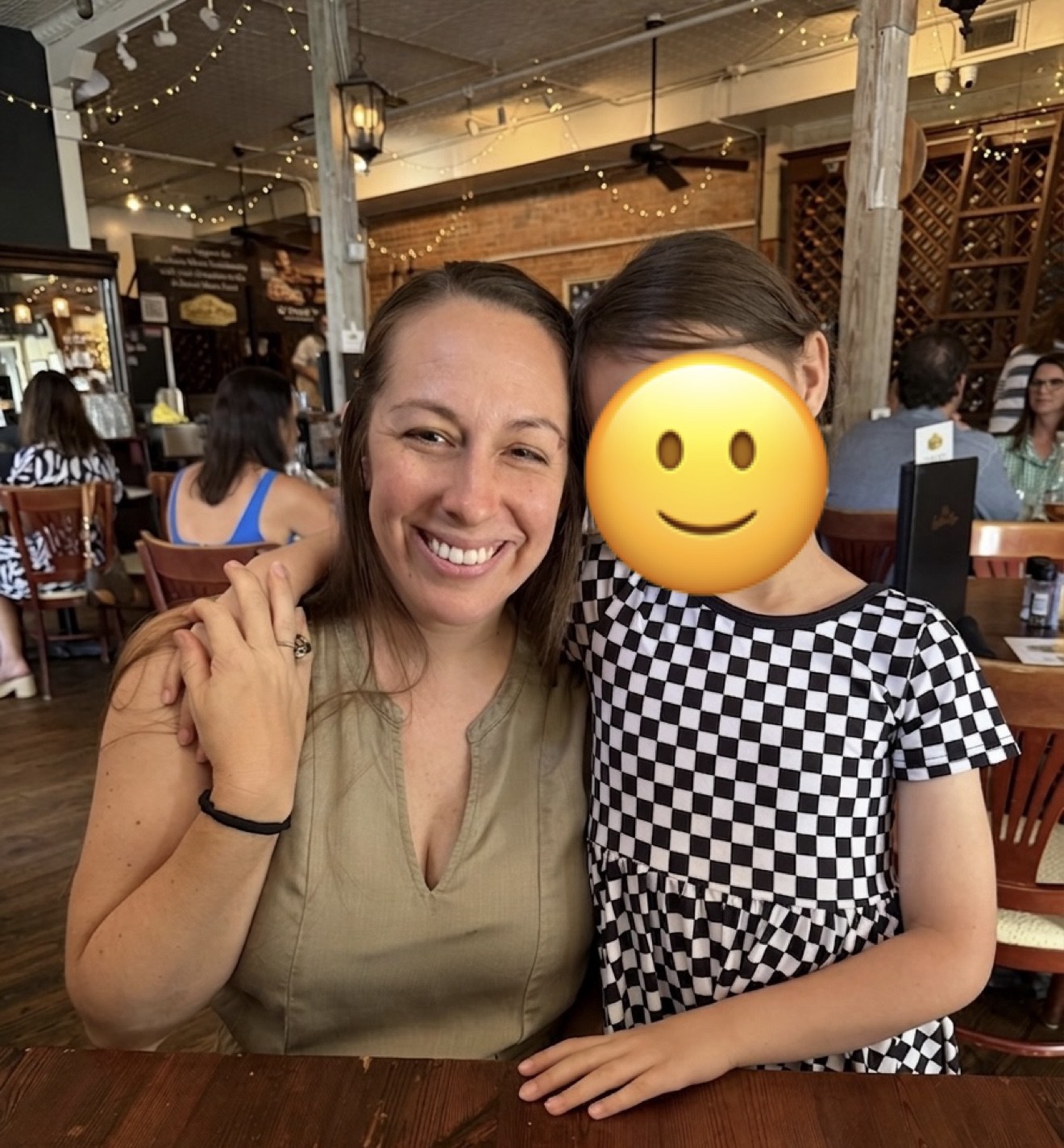 Kalena and our daughter at a restaurant with a smiley face covering our daughter’s face