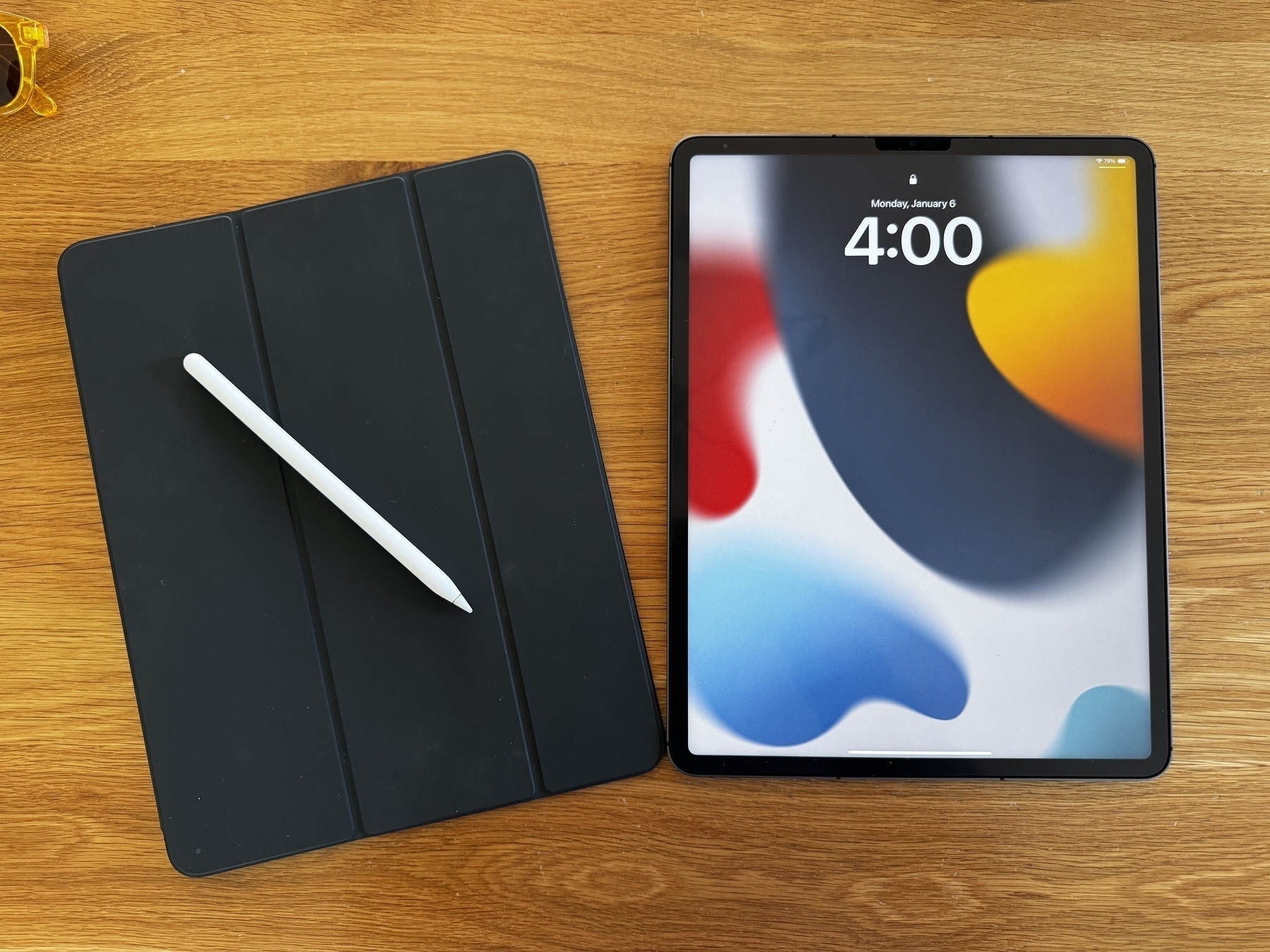 Auto-generated description: A tablet with a colorful abstract screen is placed next to a closed black cover with a stylus on top, all resting on a wooden surface.