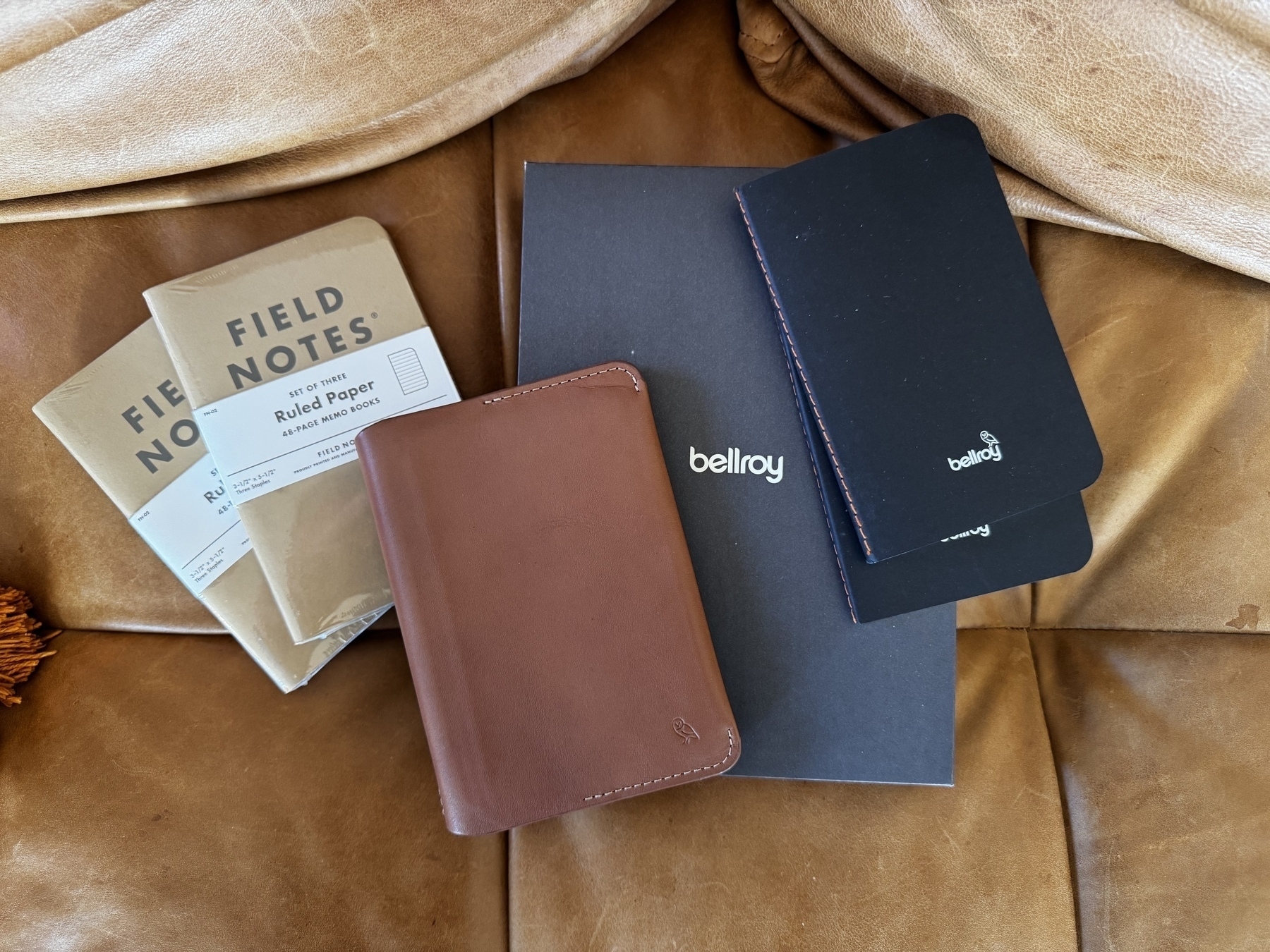 Auto-generated description: Several notebooks and a brown leather cover are arranged on a brown leather surface.